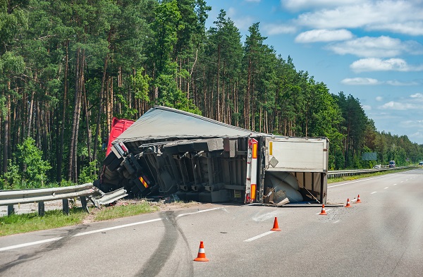 A rollover truck accident on a highway. The 18-wheeler is tipped on its side and is on the side of the road.