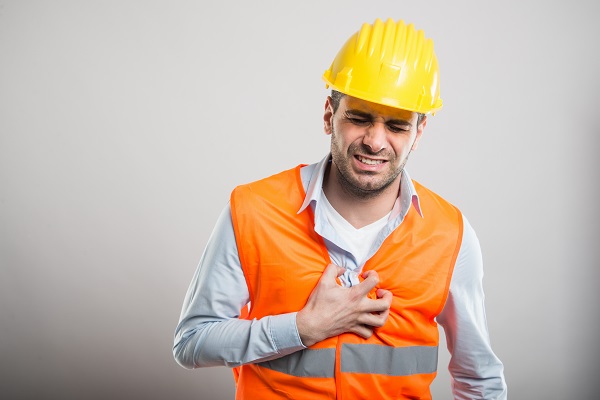 Male construction worker holding heart in pain on a gray background