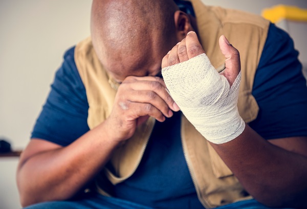 Man with a bandaged hand hunched over in pain.