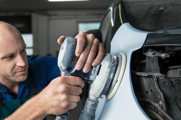 Grinder in the hands of a man who sharpen a car varnish in the car shop.