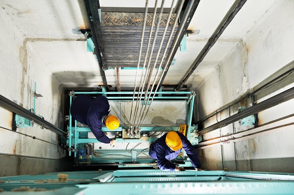 Two male technicians adjusting an elevator mechanism of lift with spanner. High angle view looking down on the workers in the elevator shaft.