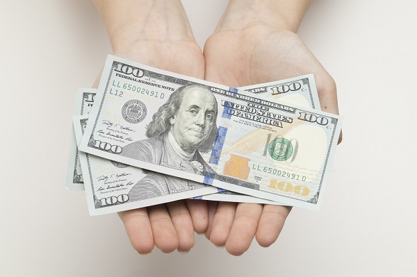 A pair of open hands holding three $100 bills in cash.