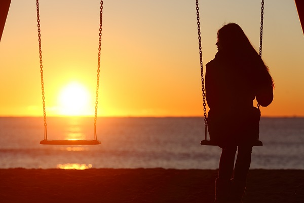 Single woman alone swinging on the beach and looking at the other empty seat