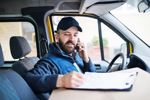 Delivery man delivering parcel box to recipient - courier service concept. A man with a smartphone making a phone call.