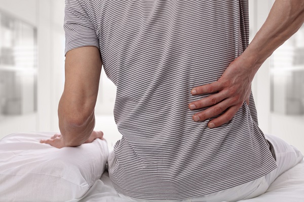 Man suffering from back pain at home in the bedroom. Uncomfortable mattress and pillow causes back pain.