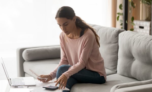 A woman sitting on a couch, using a laptop and calculator