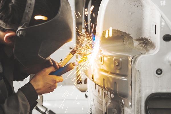 Worker in mask welds car