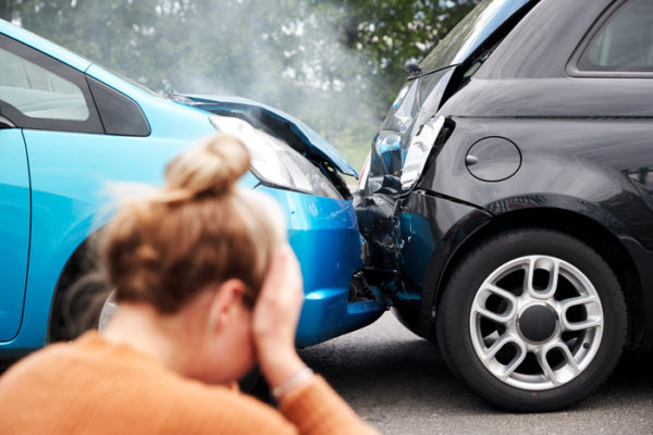 Upset woman sits on the ground with her head in her hands after a car accident.