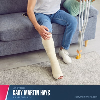 Person sitting on a couch with a fully bandaged leg, holding crutches beside them, representing a personal injury situation.