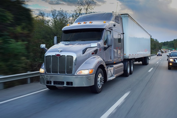 A modern gray semi-truck with a white trailer traveling down a multi-lane highway in Georgia, with other passenger vehicles visible in the distance. (179735764)