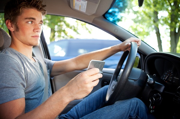 A teenage driver looking at a smartphone while holding the steering wheel, a dangerous habit highlighted during 2026 Marietta mock crash events to prevent teen distracted driving accidents across Georgia.