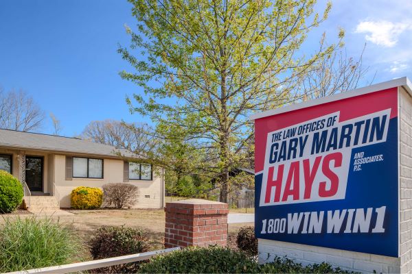Law office sign for Gary Martin Hays & Associates outside a beige office building with trees and landscaping.