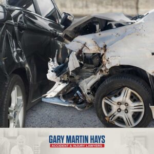 Severely damaged black sedan with a crushed hood, shattered windshield, and wrecked front bumper following a car accident.