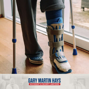 Person seated in a wheelchair wearing a black orthopedic walking boot with adjustable straps on one leg.
